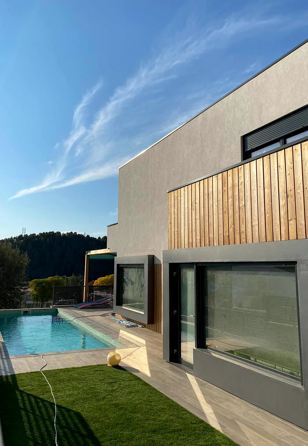 Fachada gris con revestimiento de madera y piscina en una casa de entramado ligero