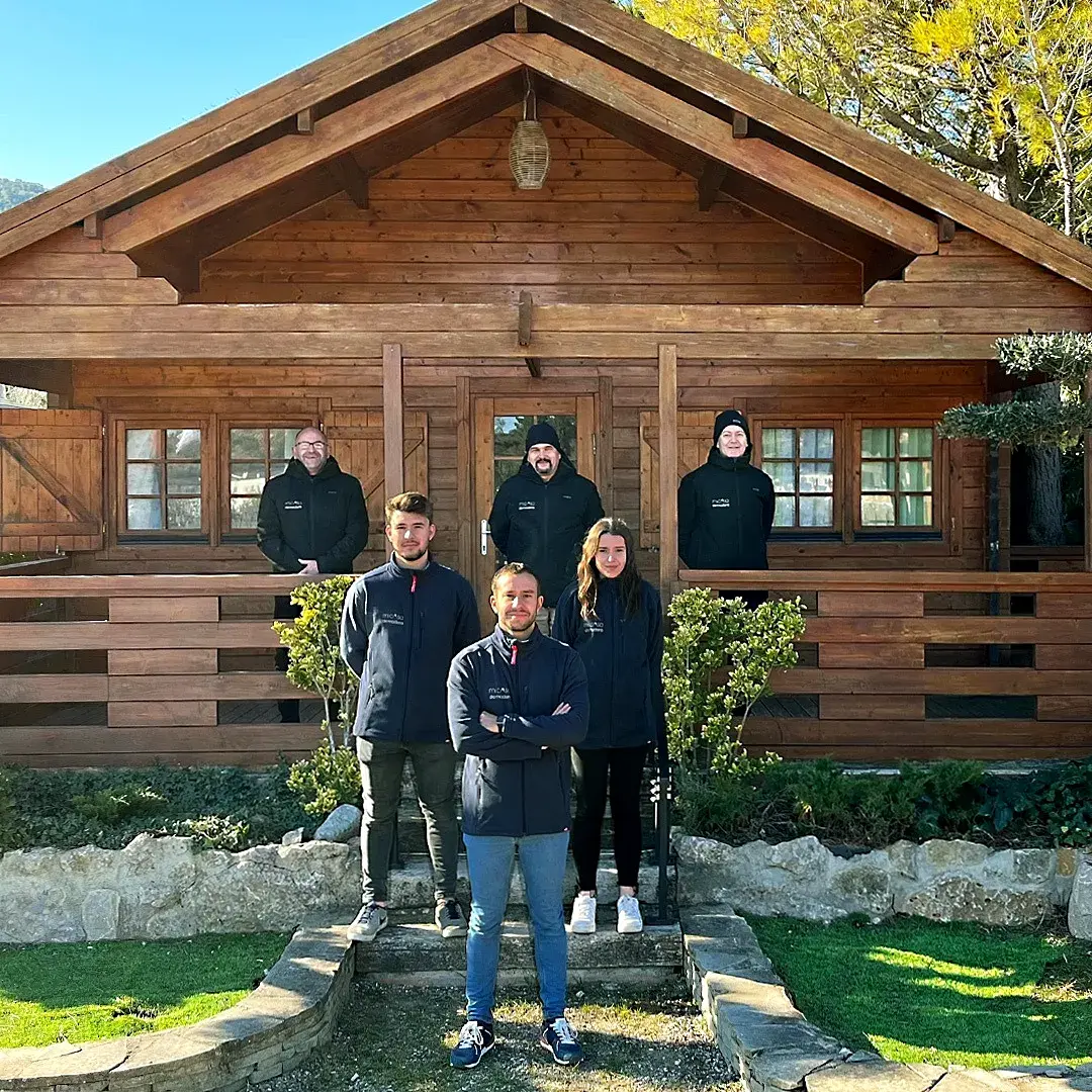 Equipo de Mi Casa de Madera delante de una casa de madera
